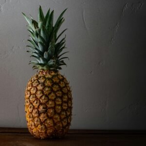 A ripe pineapple placed on a wooden surface against a textured wall, capturing its natural, fresh appeal.