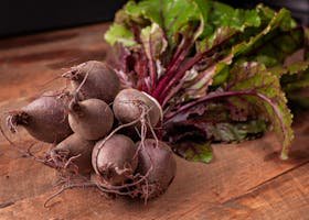 Bundle of fresh organic beetroots with vibrant green leaves on a wooden surface.