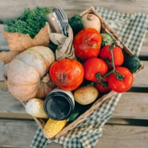 A top-down view of a basket filled with fresh vegetables and produce, placed on a wooden table.