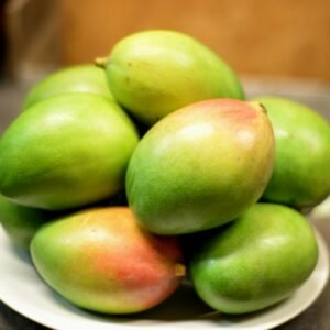 Vibrant green mangoes on a white plate, showcasing freshness and juiciness.
