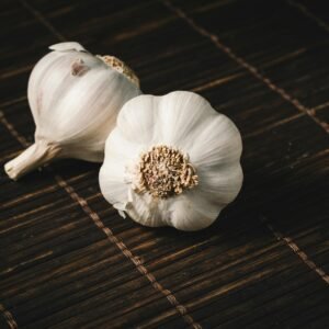 Two fresh garlic bulbs on a dark wooden mat, highlighting aromatic culinary ingredients.